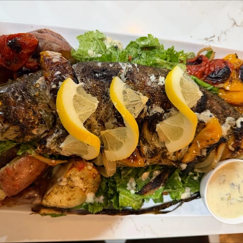 Lake trout bake with roasted potatoes, vegetables, lemon slices, and lemon caper cream sauce.