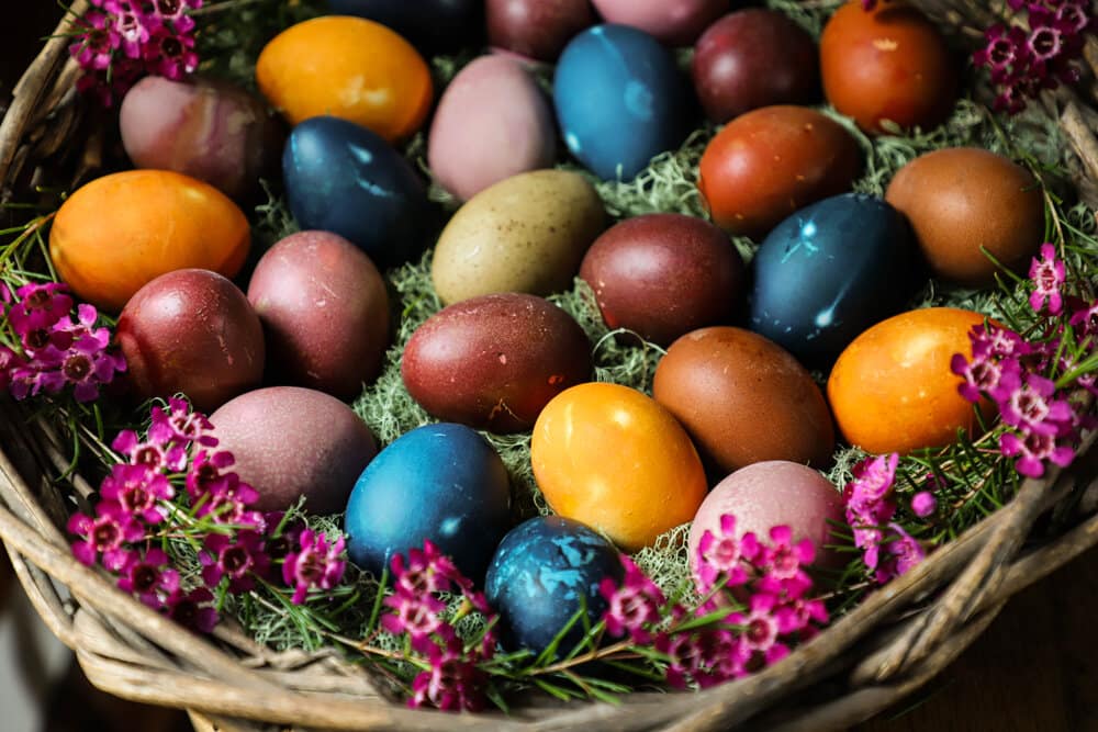 Basket of naturally dyed Easter eggs in vibrant colors surrounded by pink flowers