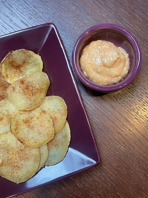 Thinly sliced potatoes stacked neatly with a creamy plant-based sauce on the side.