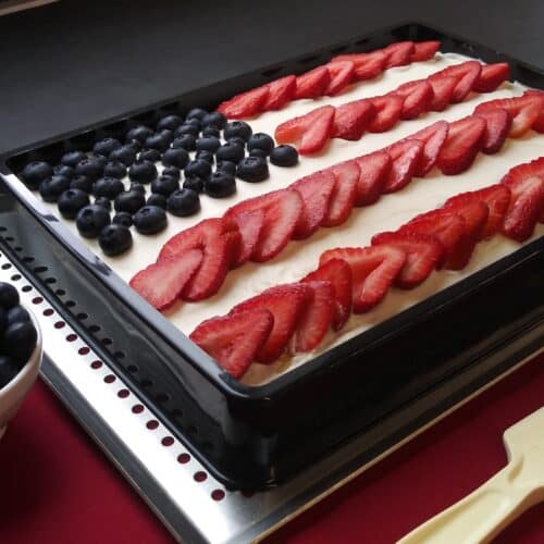 Rectangular cake decorated as an American flag with strawberries and blueberries in a black rectangular mold.