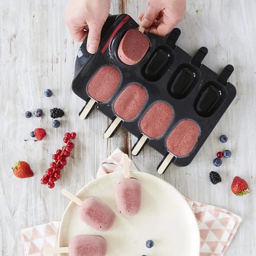 Gourmet popsicles being removed from FORTEEZ Popsicle Tray, surrounded by fresh berries on a white wooden table.