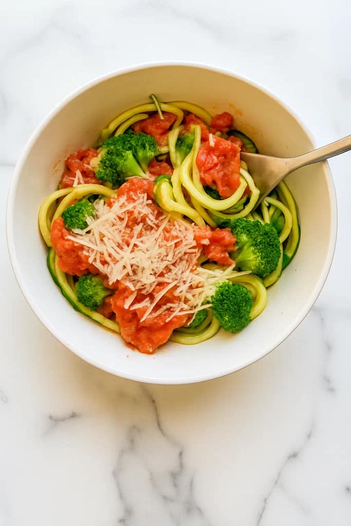 Oven-baked zoodles with broccoli and marinara sauce topped with Parmesan cheese in a white bowl