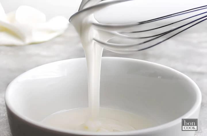 White glaze being poured from a whisk into a bowl for finishing Base & Bloom mini loaf cakes.
