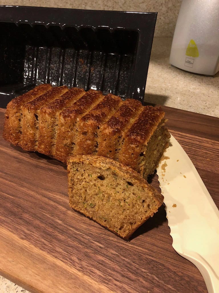 Sliced banana bread loaf on a wooden cutting board with a serrated knife, baked in a rectangular loaf mold.