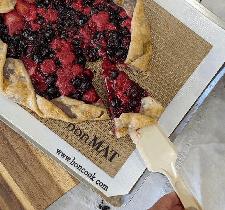 Rustic mixed berry galette with golden crust and vibrant strawberries, blueberries, and raspberries, freshly baked on parchment paper.
