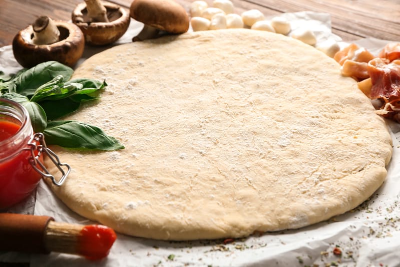 Homemade pizza dough on a floured surface with fresh basil and toppings