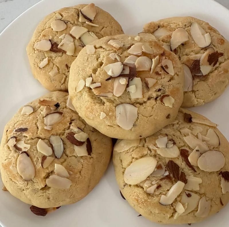 "Golden-brown Greek almond cookies infused with orange blossom water, arranged on a rustic ceramic plate with scattered almonds and orange zest."